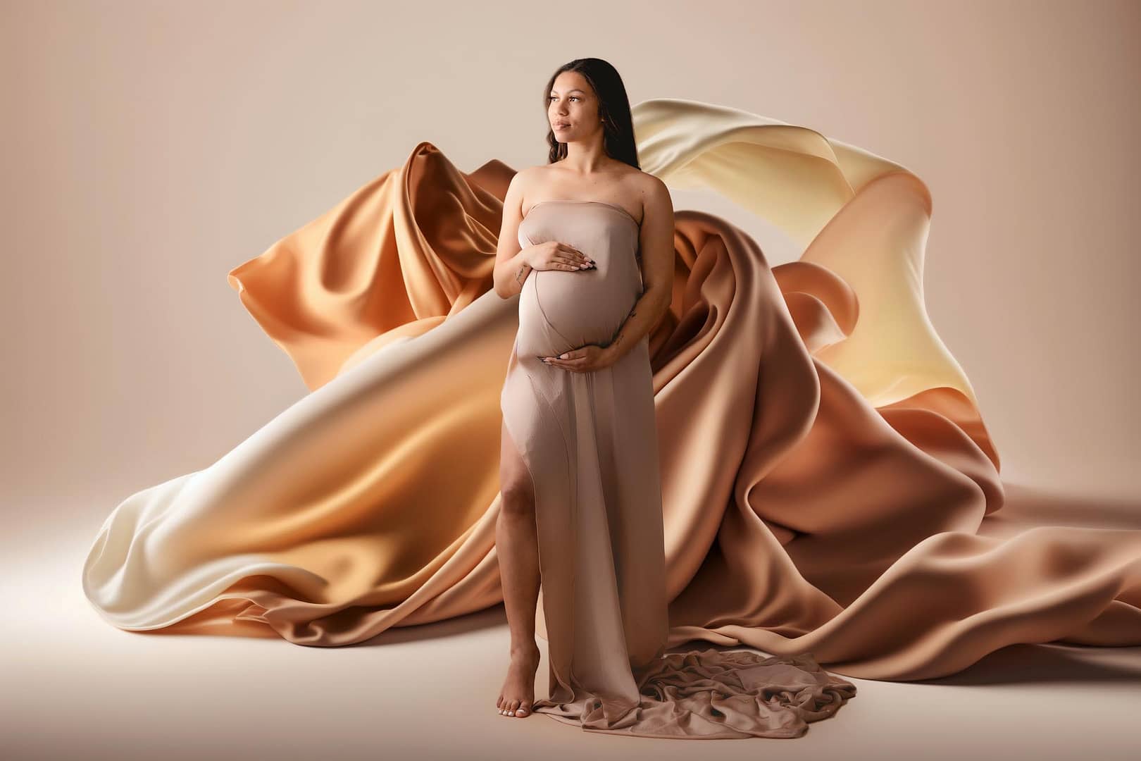 Mom to be wearing a gold colored fabric draped over belly with fabric flowing behind her captured by a maternity photographer in San Diego