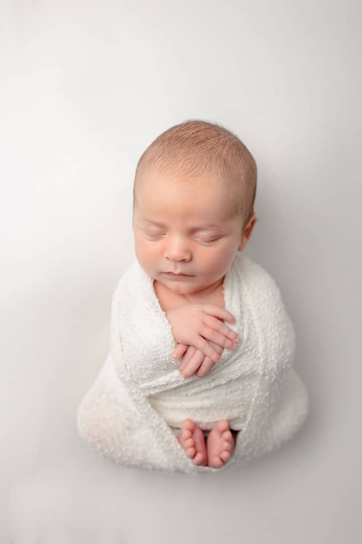 Newborn Baby wrapped in white on white backdrop for newborn pictures