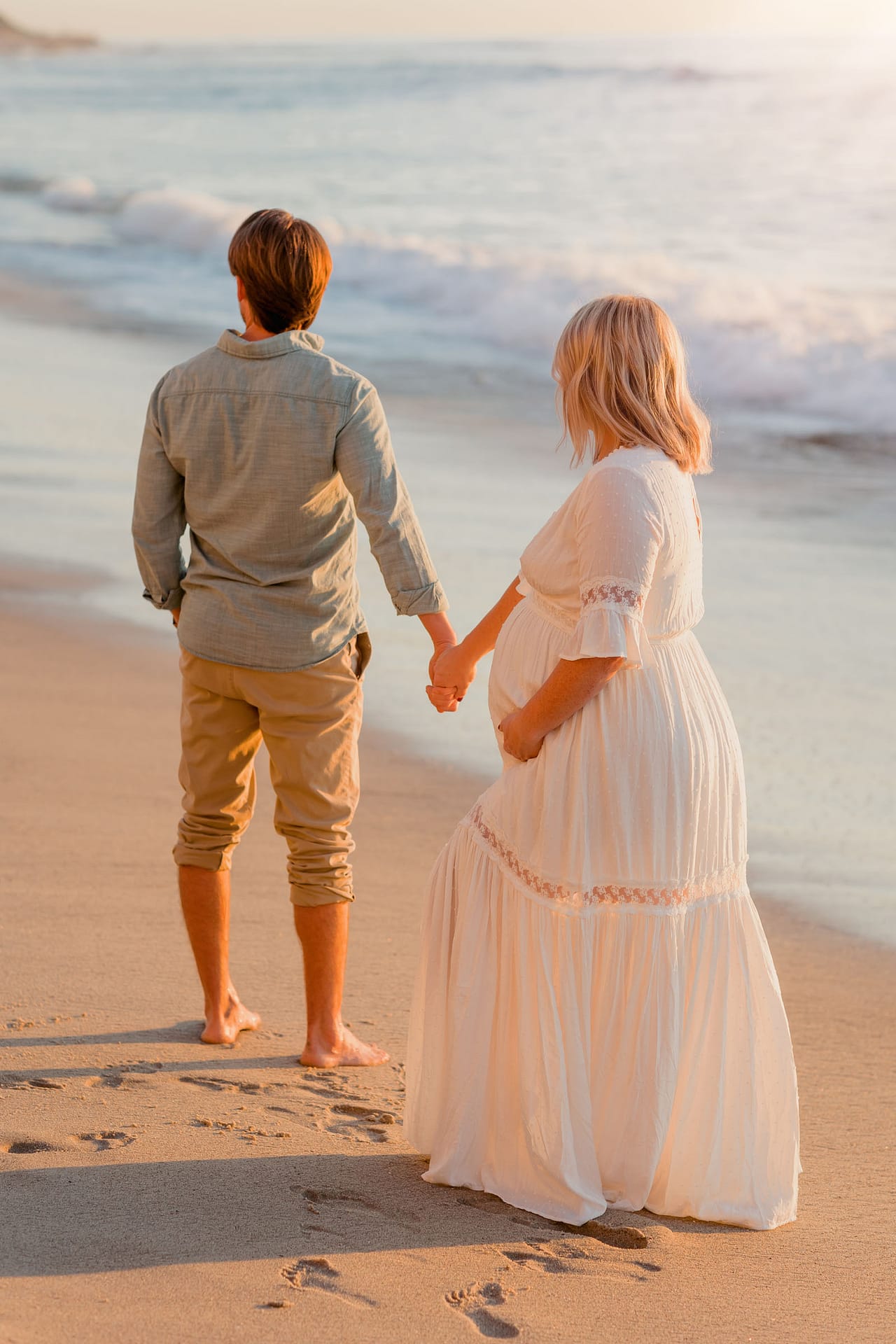Pregnant Mom and Dad to be holding hands during golden hour sunset on La Jolla Beach