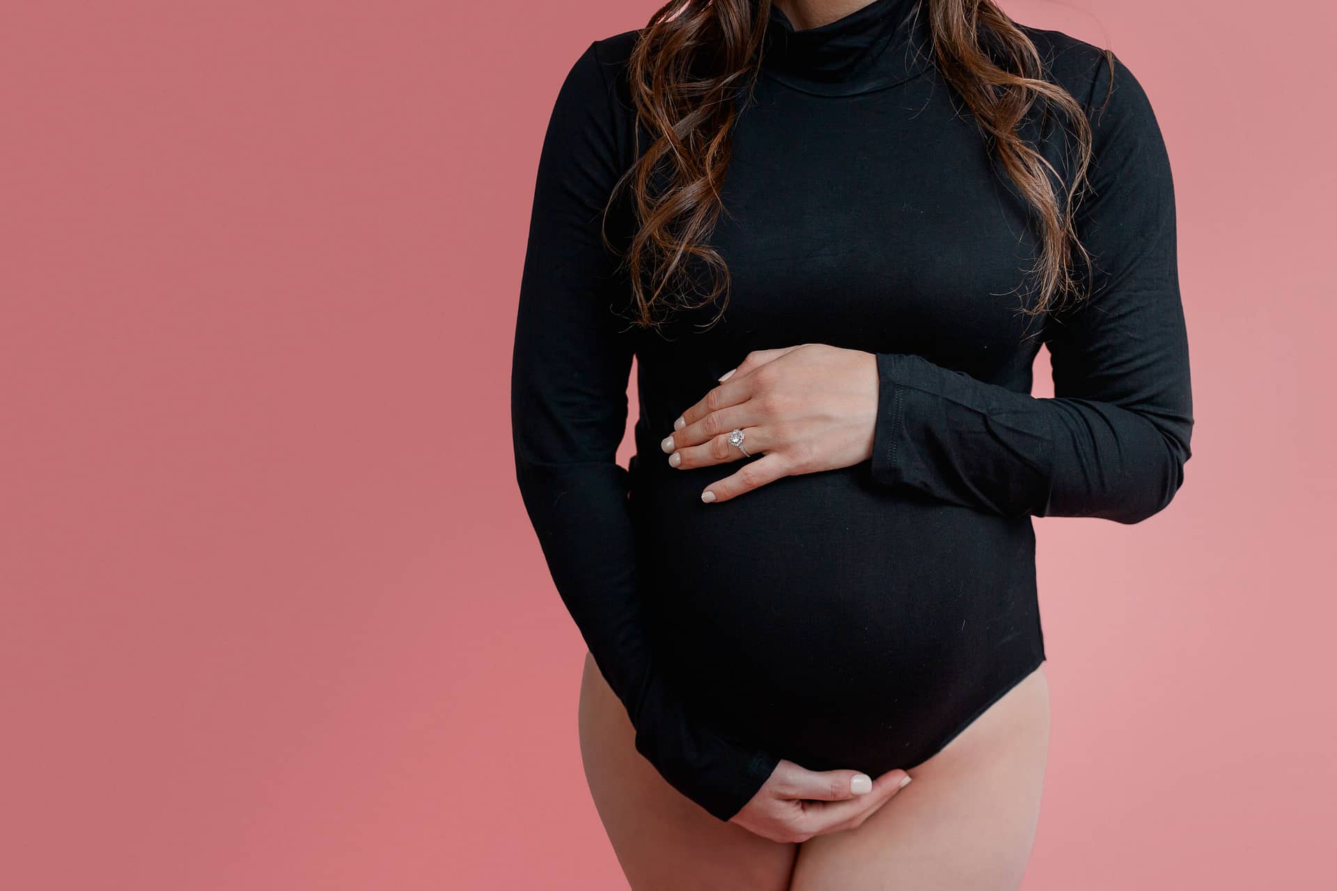Close up of pregnant mom in black bodysuit on pink backdrop